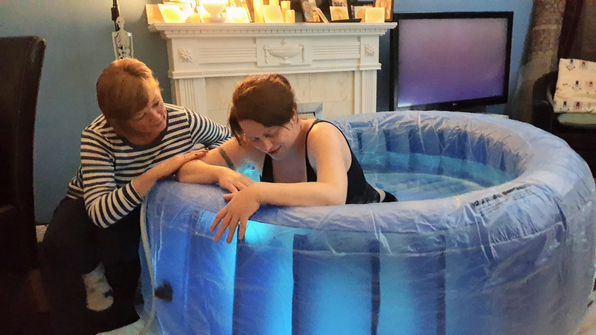 Woman labouring in birth pool with doula comforting her